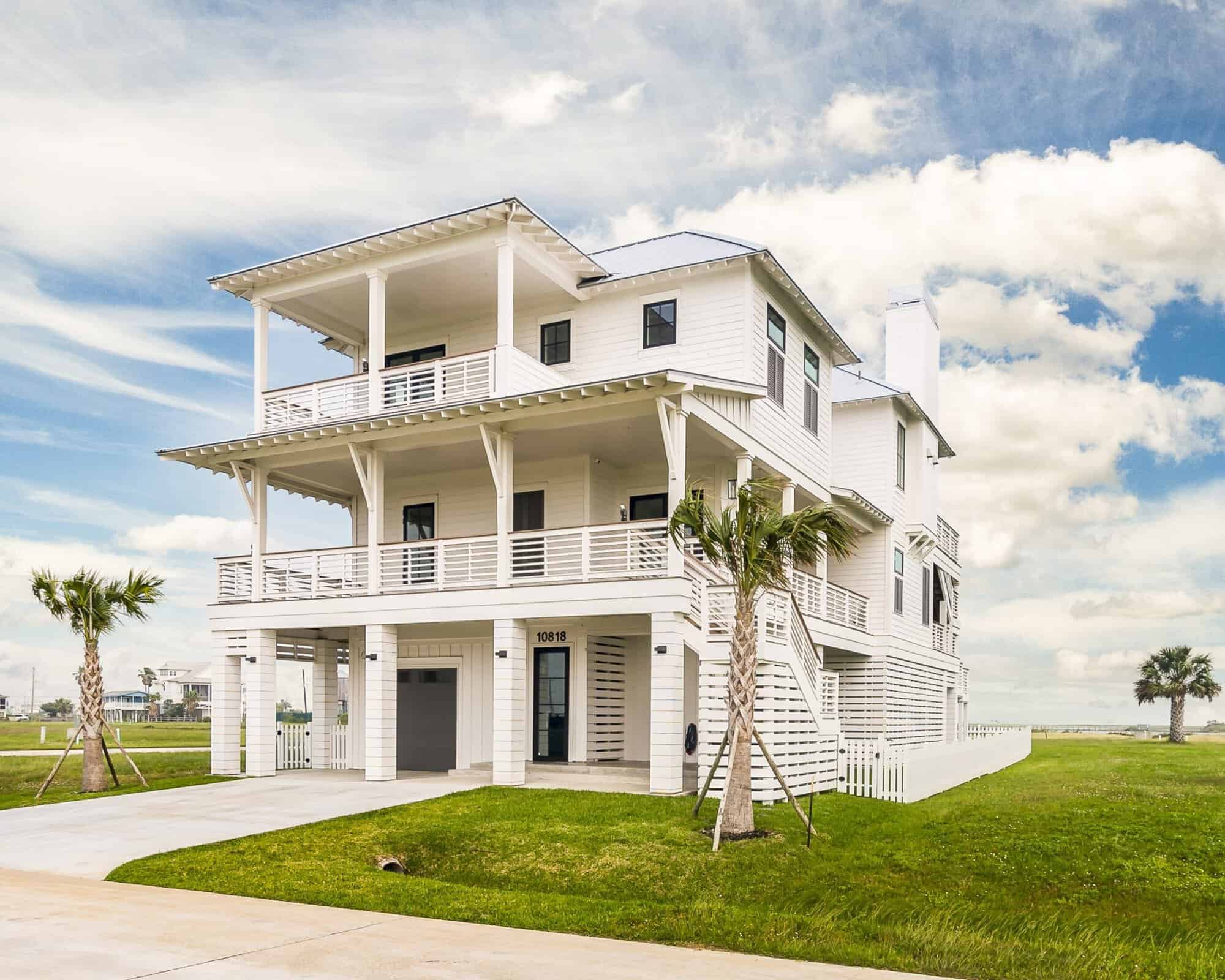 White three-story elevated coastal home with a standing seam metal roof and wrap-around covered porches