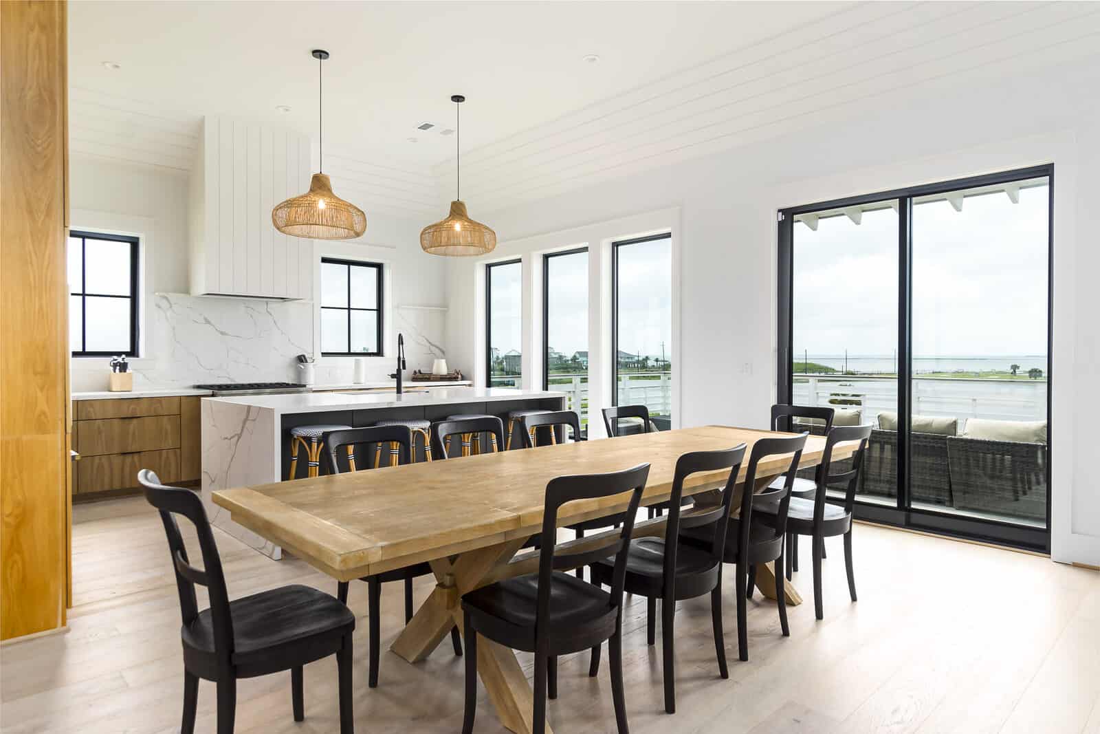 Custom coastal kitchen and dining great room with a marble waterfall island, rattan pendants and sliding doors to a bay view