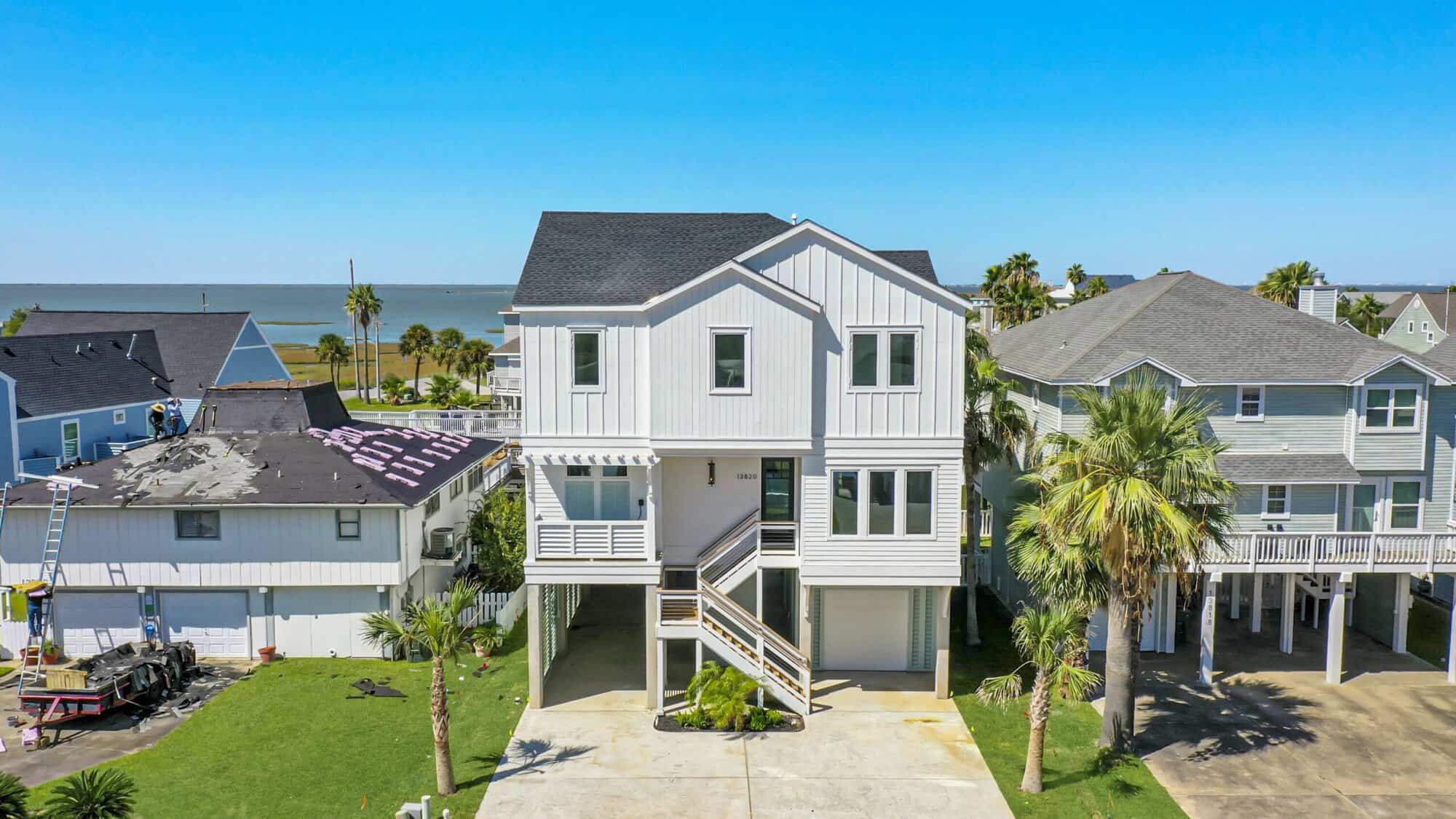 Aerial view of an elevated coastal home built on pilings with open space beneath, overlooking the bay