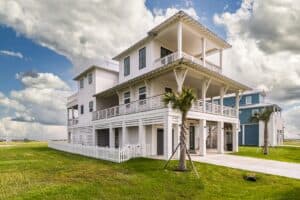 Homepage Three-quarter view of a custom white elevated beach house with covered porches, concrete driveway and ground-level garage