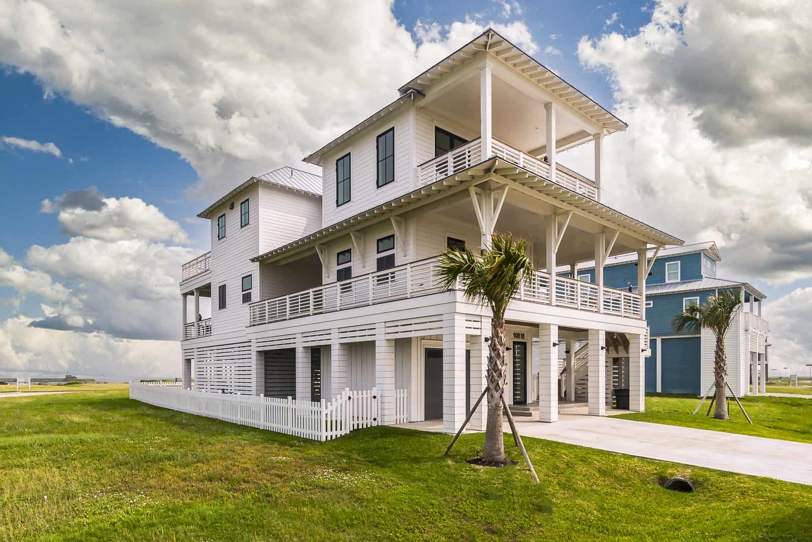 Three-quarter view of a custom white elevated beach house with covered porches, concrete driveway and ground-level garage