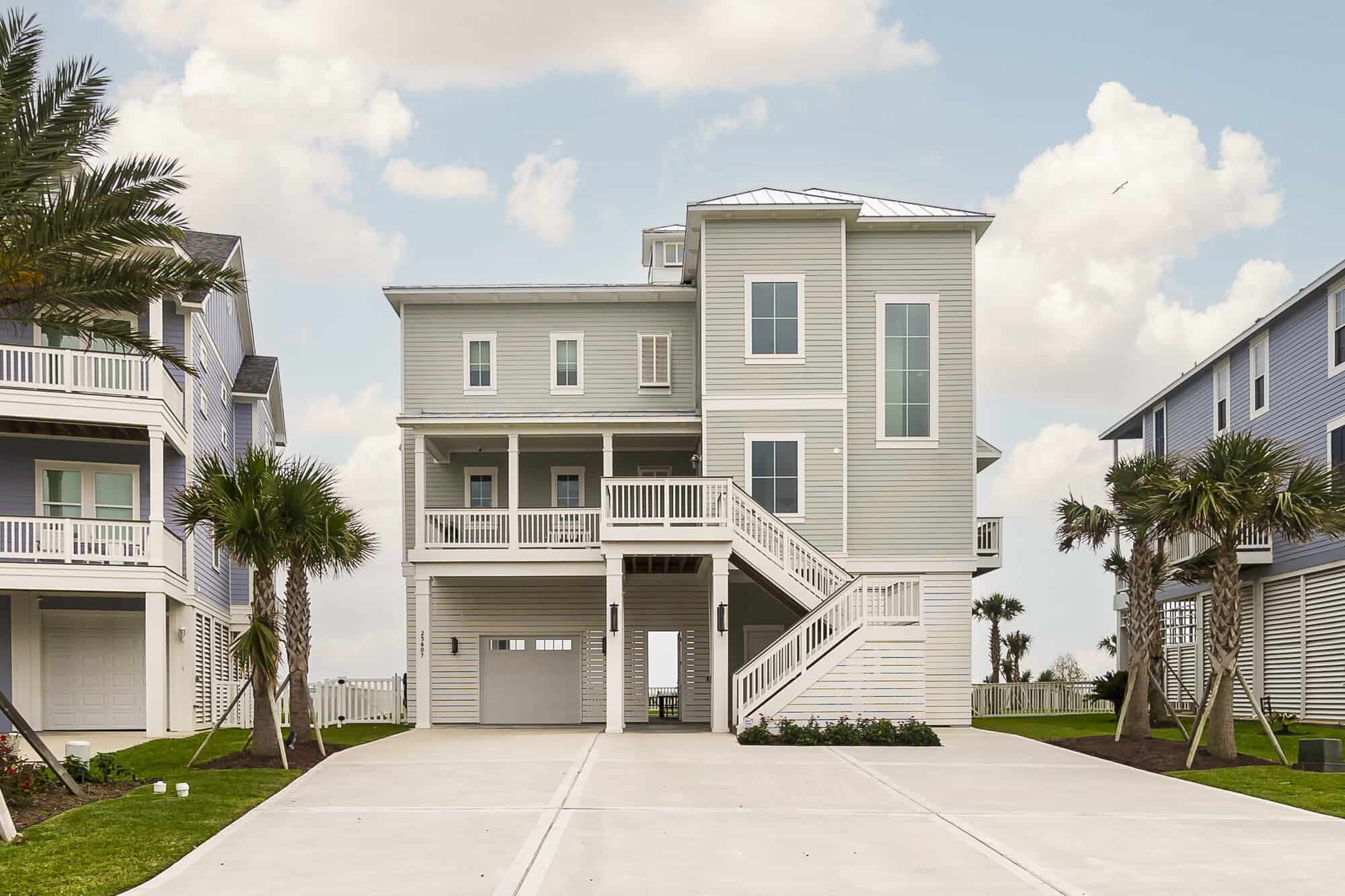 Elevated custom coastal home built on pilings with entry staircase and ground-level garage on Galveston Island