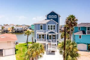 Homepage Navy three-story coastal home elevated on pilings in a FEMA flood zone, with entry stairs and covered porches above the flood level