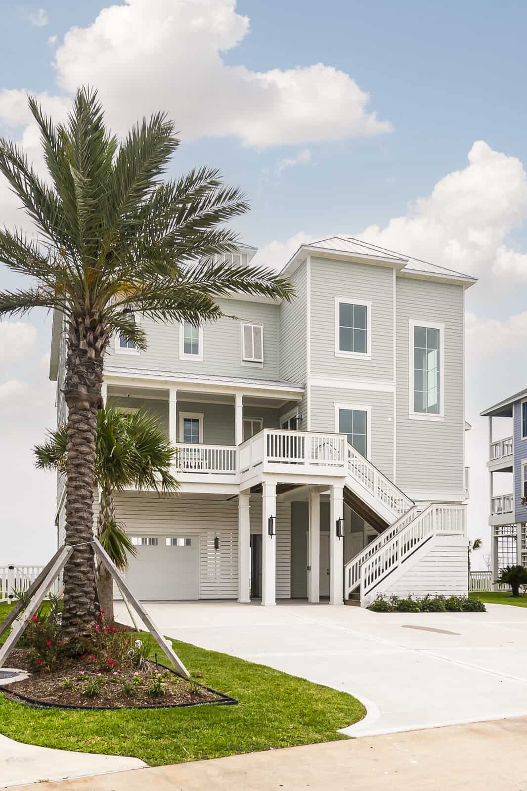 Three-story elevated coastal home with the finished floor raised well above grade, showing piling height, entry staircase and ground-level garage