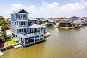 Homepage Aerial view of a three-story canal-front stilt home with a private dock, built by Kai Custom Homes in Jamaica Beach, Texas