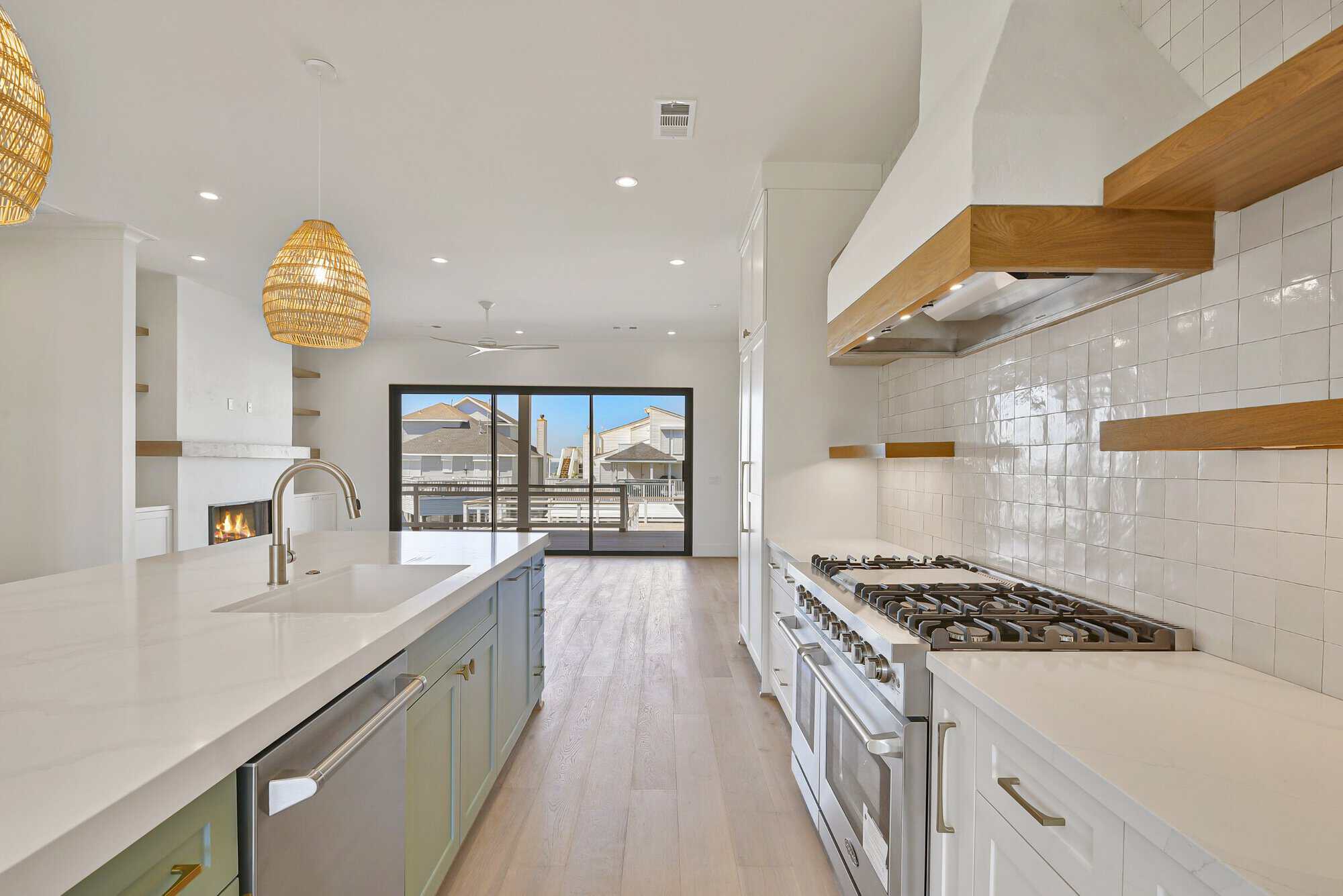 Kitchen with a white quartz island, sage cabinetry, professional gas range and zellige tile in a Kai Custom Homes build in Pirates Cove, Galveston