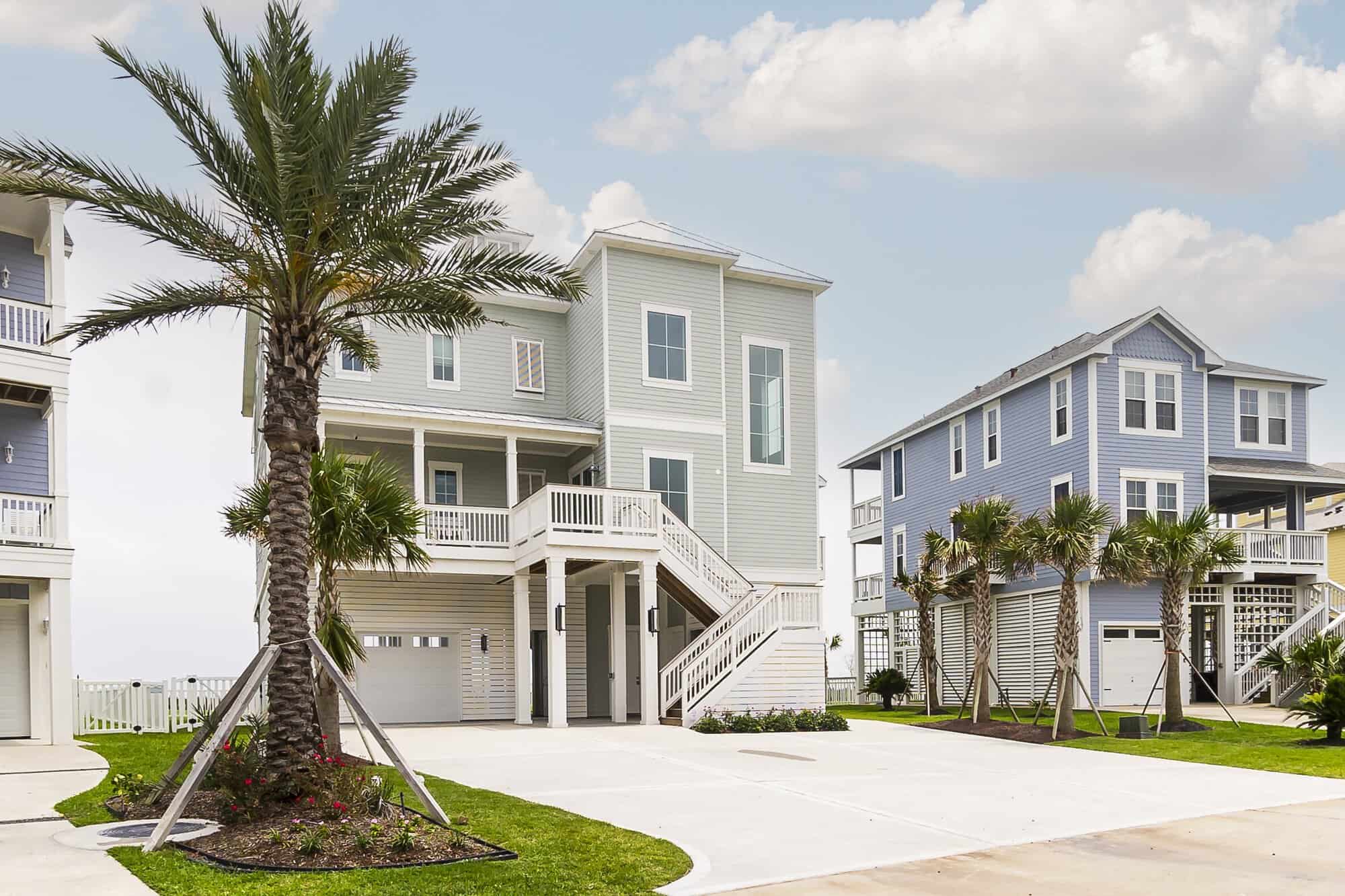 Elevated beach home with a date palm, driveway and double entry stairs, built by Kai Custom Homes in Pointe West, Galveston