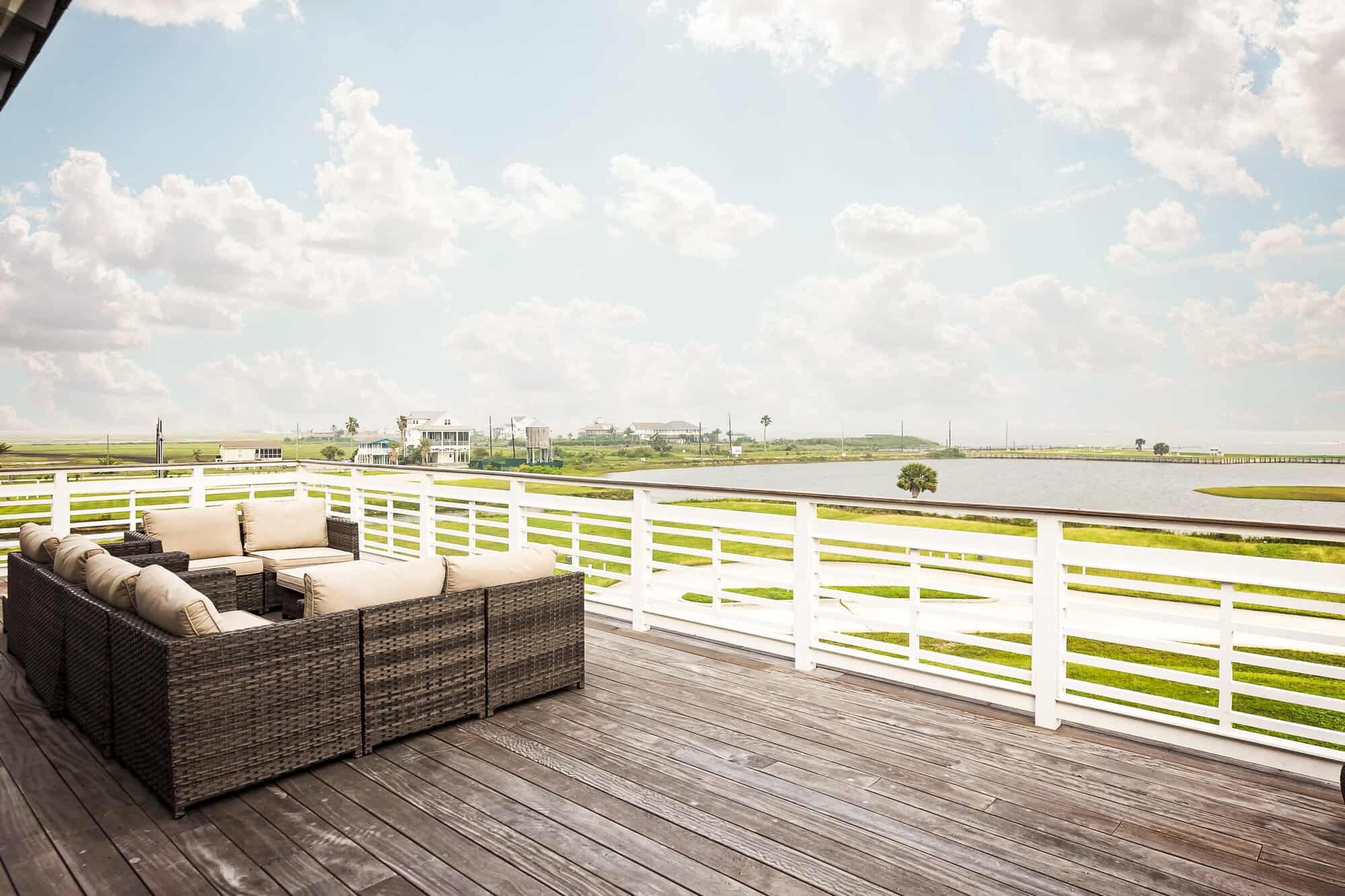 Upper deck with wicker seating overlooking marsh grass and West Bay at a Kai Custom Homes build in Sweetwater Cove, Galveston